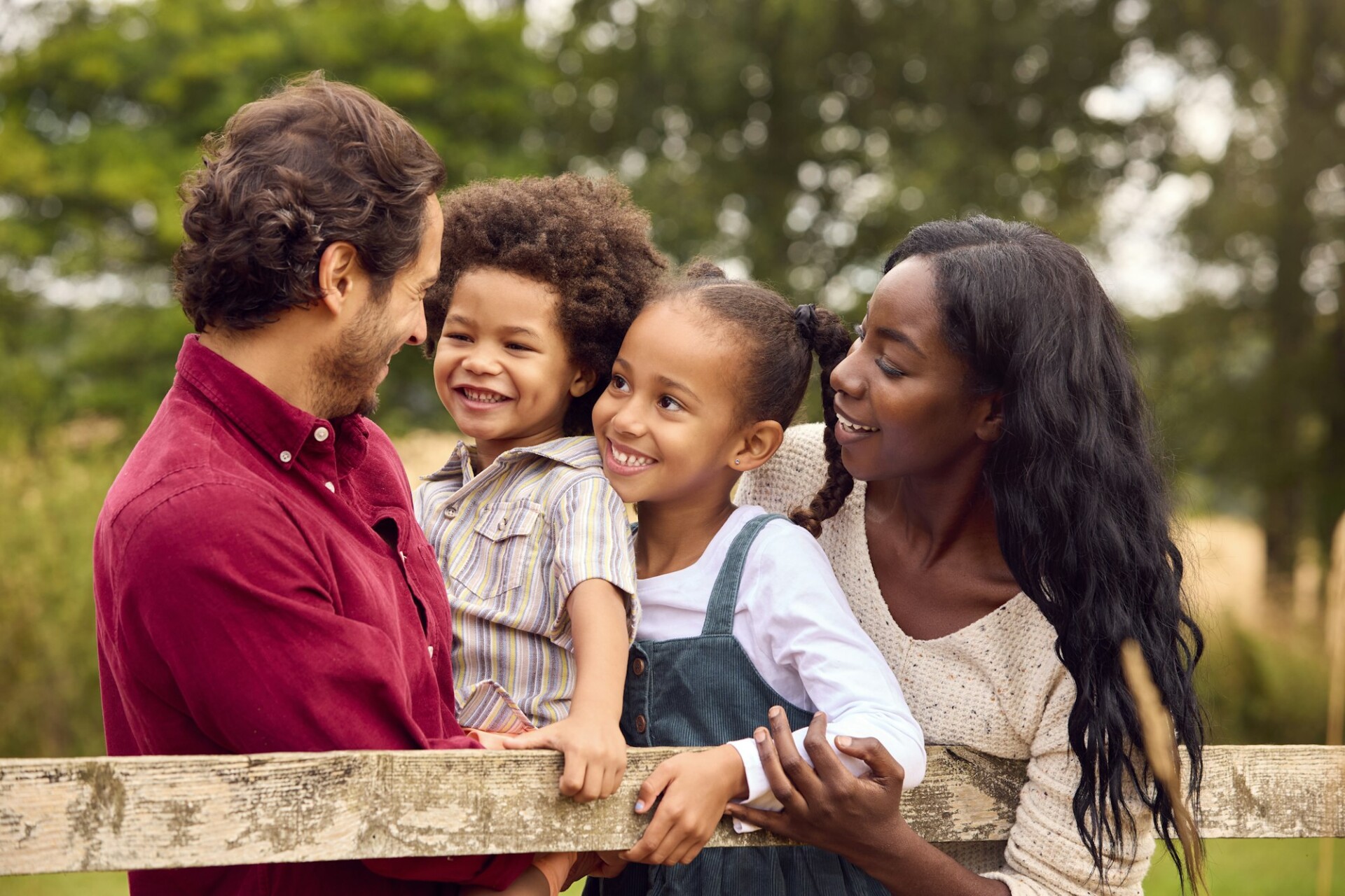 Loving Mixed Race Family Leaning On Fence On Walk In Countryside